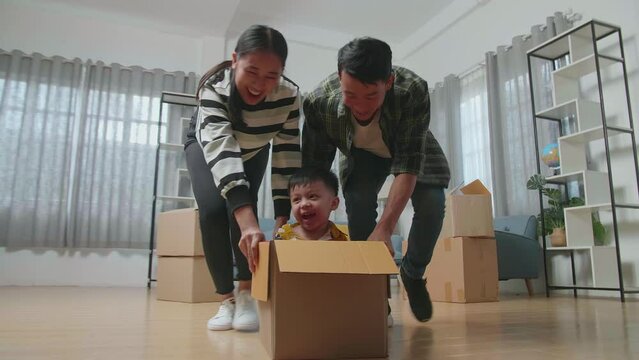 Happy Asian Family Having Fun With Cardboard Box After Moving Into A New House. They Celebrate Moving Day 
