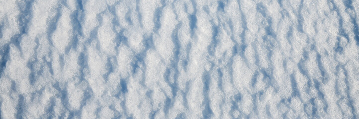 Fototapeta premium Beautiful winter background with snowy ground. Natural snow texture. Wind sculpted patterns on snow surface. Wide panoramic texture for background and design.