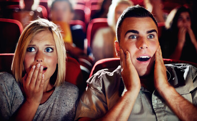 Couple watch a scary, horror or thriller movie in a cinema together and are shocked, wow or...