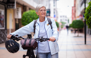 Senior cyclist woman pushing her electric bicycle in urban street. Active elderly grandmother...