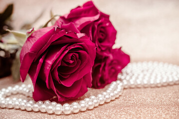Red rose and pearl necklace on a shiny gold background
