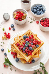 Traditional belgian waffles with fresh berries, raspberries, currant, blueberries, maple syrup, thyme on pink background. Summer concept. Selective focus.