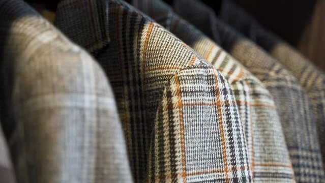 Grey patterned tweed jackets hanging in wooden wardrobe, close up.