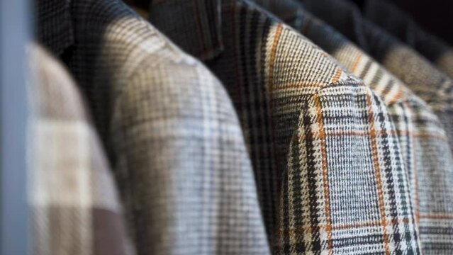 Patterned tailored tweed jackets hanging in wooden wardrobe, close up.