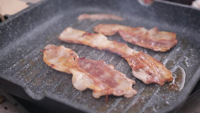 cooking Pieces of flavorful sliced organic bacon fried in grill pan