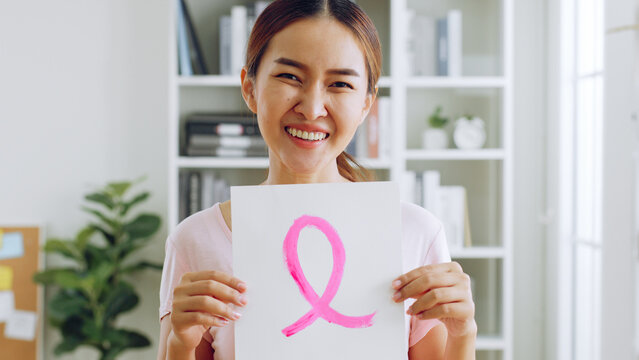 Smiling young Asian woman show pink ribbon sign as sign of October Breast Cancer Awareness month