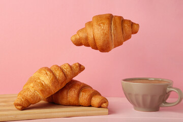 Flying croissant with coffee on pink background.