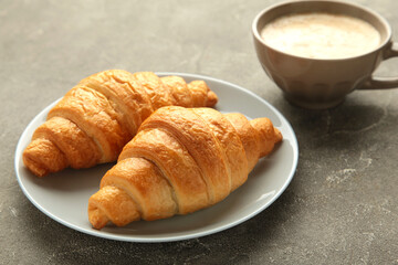 Two french croissants on plate and cup of coffee on concrete background.