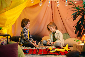Obraz na płótnie Canvas Two young boys with long hair are high fiving each other and seem really happy to be in an indoor tent