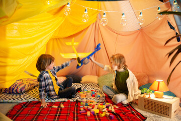 Obraz na płótnie Canvas Two best buddies are playing in an indoor blanket tent with airplanes, all while enjoying each others presence