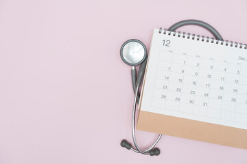 Top view of stethoscope and calendar on the pink table background flat lay, schedule to check up...