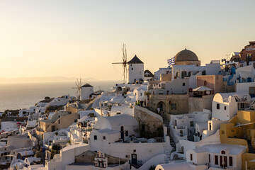 Whitewashed houses and windmills in Oia in warm rays of sunset on Santorini island. Greece