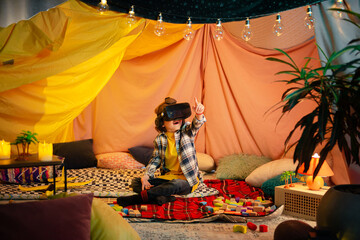 Obraz na płótnie Canvas The boy are inside a massive and brightly colored indoor blanket fort while playing together with a vr headset