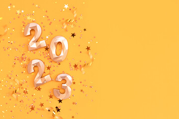 2023 golden numbers, stars confetti and ribbons on a bright yellow background. New Year's concept with copy space.