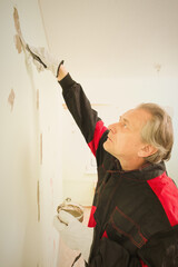 Older man working in empty apartment repairing holes in walls