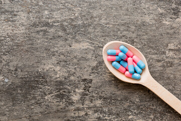 Vitamin capsules in a spoon on a colored background. Pills served as a healthy meal. Red soft gel vitamin supplement capsules on spoon