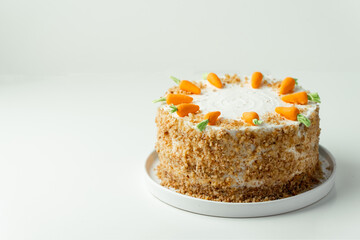 Delicious carrot cake decorated with mastic sweet carrots. Homemade carrot cake with yellow crumbs in the white plate on the white background