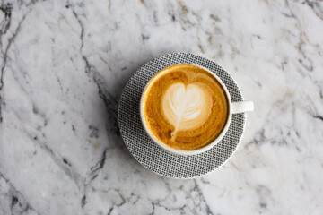 Trendy pink cup of hot cappuccino on marble table background. Heart shape latte art for symbol of love. One cup for morning routine.