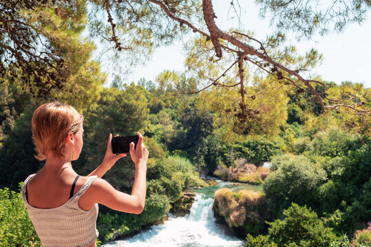 Beautiful teenage girl taking photo of waterfall. Krka waterfalls National park, Croatia
