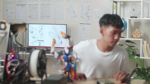 Asian Boy Walking To Look At The Pictures On The Wall While Working About A Cyborg Hand At Home
