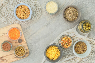 Set of vegetarian organic products in glass jars and bowls on a white wooden background. Top view, copy space.