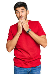 Young handsome man wearing casual red tshirt laughing and embarrassed giggle covering mouth with...