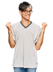 Young hispanic man wearing casual clothes and glasses very happy and excited doing winner gesture with arms raised, smiling and screaming for success. celebration concept.