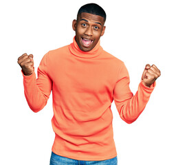 Young black man wearing orange turtleneck sweater screaming proud, celebrating victory and success very excited with raised arms