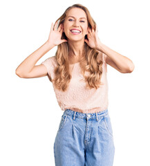 Young beautiful caucasian woman with blond hair wearing casual clothes trying to hear both hands on ear gesture, curious for gossip. hearing problem, deaf