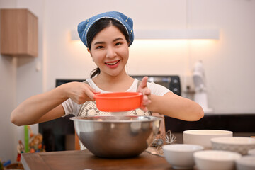 Beautiful Asian female is preparing her cupcake flour with a flour sifter.