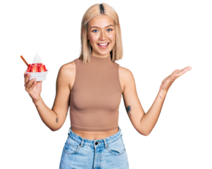 Beautiful young blonde woman eating strawberry ice cream celebrating achievement with happy smile and winner expression with raised hand