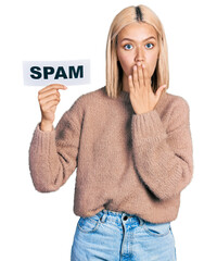 Beautiful young blonde woman holding spam banner covering mouth with hand, shocked and afraid for...