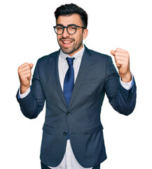 Hispanic man with beard wearing business suit and tie screaming proud, celebrating victory and success very excited with raised arms