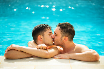 Gay couple relaxing in swimming pool. LGBT. Two young men enjoying nature outdoors, kissing and hugging. Young men romantic family in love. Happiness concept.
