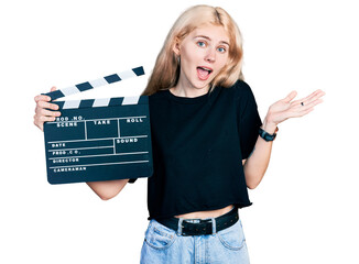 Young caucasian woman holding video film clapboard celebrating achievement with happy smile and...