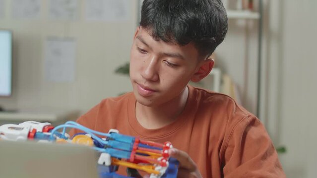 Close Up Of Asian Boy Checking And Comparing A Cyborg Hand To The Picture On A Laptop At Home While At Home
