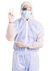 Young hispanic man wearing doctor protection coronavirus uniform and medical mask smiling with happy face winking at the camera doing victory sign. number two.