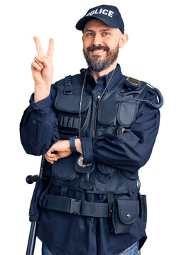 Young handsome man wearing police uniform smiling with happy face winking at the camera doing victory sign with fingers. number two.