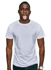 Young african american man wearing casual white t shirt sticking tongue out happy with funny expression. emotion concept.