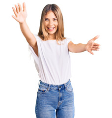 Fototapeta na wymiar Beautiful caucasian woman with blonde hair wearing casual white tshirt looking at the camera smiling with open arms for hug. cheerful expression embracing happiness.