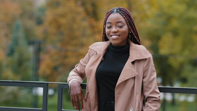Happy joyful young african american woman standing in autumn park attractive stylish confident successful businesswoman looking at camera smiling healthy white teeth beautiful model posing outdoors