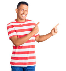 Young handsome latin man wearing casual clothes smiling and looking at the camera pointing with two hands and fingers to the side.