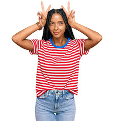 Beautiful hispanic woman wearing casual clothes doing funny gesture with finger over head as bull horns