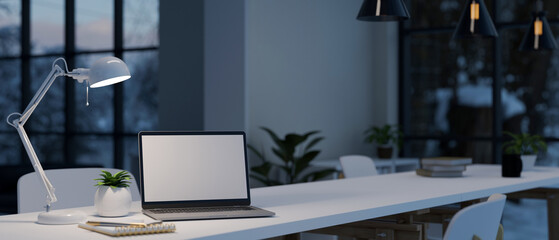 Office workspace in the evening with a notebook laptop mockup, table lamp on white table.