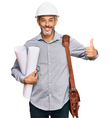 Middle age grey-haired man wearing safety helmet holding blueprints smiling happy and positive,...