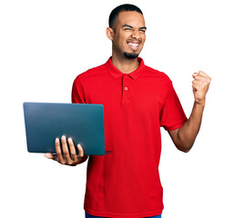 Young african american man working using computer laptop screaming proud, celebrating victory and success very excited with raised arms