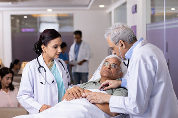 Doctors checking heartbeat of patient using stethoscope lying on hospital bed
