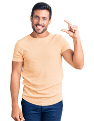 Young hispanic man wearing casual clothes smiling and confident gesturing with hand doing small size sign with fingers looking and the camera. measure concept.