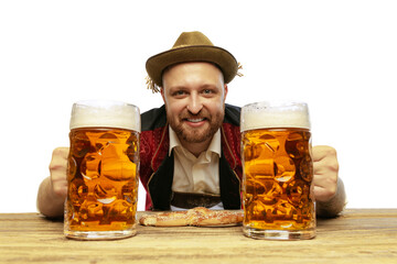 Portrait of young man wearing traditional Bavarian or German clothes serving big mugs with foamy lager beer isolated over white background