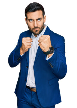 Young hispanic man wearing business jacket ready to fight with fist defense gesture, angry and upset face, afraid of problem